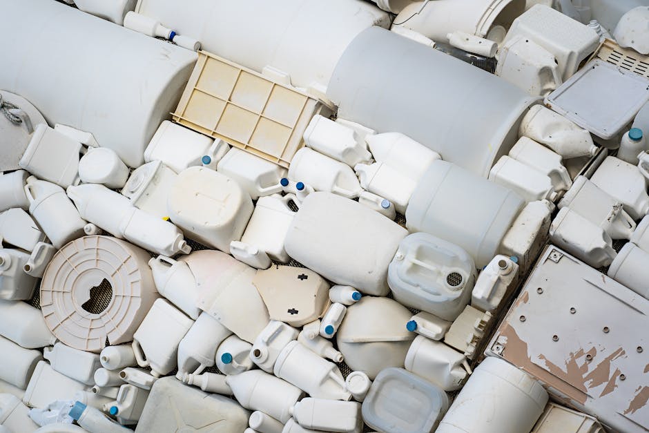 A black cylindrical trash bin placed against a large beige tiled wall inside a building, filled with various food containers, disposable packaging, and wrappers, with some rubbish overflowing onto the